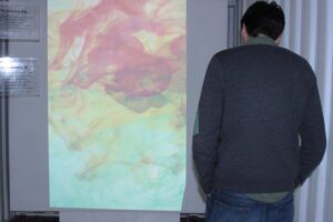 Person speaking into mic to make unique digital composite painting of colored ink drops projected on a canvas screen